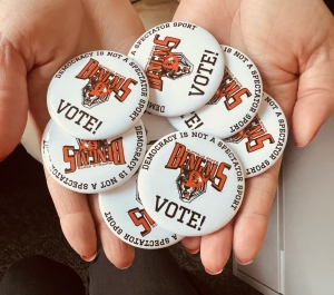 A pile of buttons that say "Democracy is not a spectator sport" and Buffalo State Bengals logo, along with Vote!