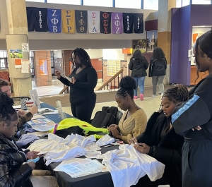 Photo of students sitting at a table creating reusable bags out of old t-shirts.