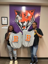 Two students holding finished t-shirt bags in front of a Bengal poster